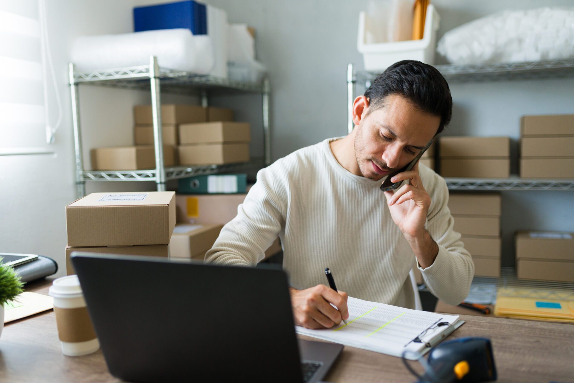 Latin entrepreneur taking notes while talking on the phone with a customer and managing orders in his small business store